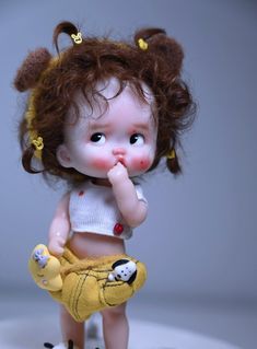 a close up of a small doll on a white surface with one hand in her mouth