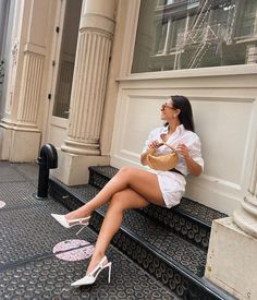 a woman sitting on a bench in front of a building wearing high heels and a white shirt