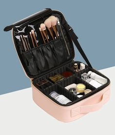 an open makeup case with brushes and other items inside it on a white table next to a blue wall