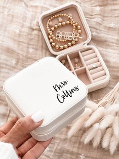 a person holding a small white box with jewelry in it on top of a bed