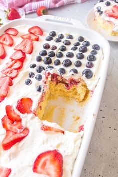 a cake with strawberries and blueberries on top in a white baking dish next to another one