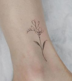 a small flower tattoo on the ankle is shown in black and grey ink, with delicate details