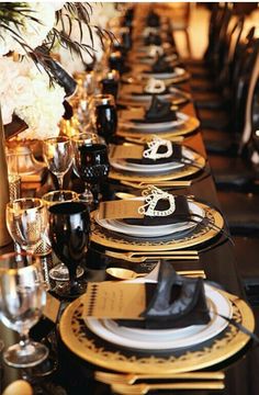 a long table is set with black and gold place settings for formal dinnereons