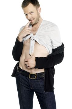 a man with no shirt on is holding his tie up to his chest and looking at the camera