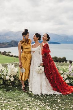 two women in dresses standing next to each other with flowers on the ground behind them