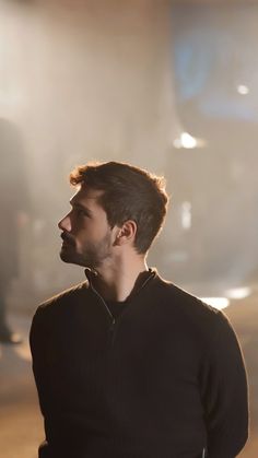 a man standing in front of a light with his head turned to the side, wearing a black sweater