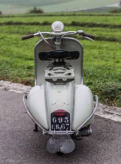 an old scooter is parked on the side of the road in front of a grassy field