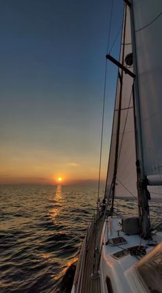 the sun is setting over the ocean on a sailboat