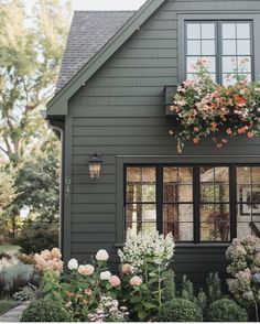 a gray house with flowers in the window boxes and plants growing on the windowsill