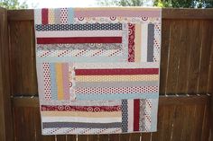 a patchwork quilt hanging on a wooden fence