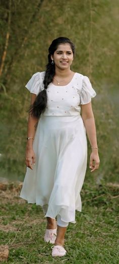 a woman in a white dress is walking through the grass