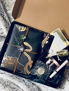 an open gift box on top of a bed next to a pen and eyeglasses