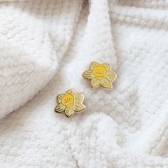 two small yellow flowers are sitting on a white blanket, next to a pair of gold - plated earrings