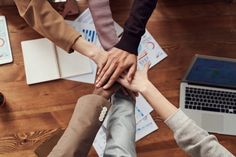 several people holding hands in the middle of a table with laptops and papers on it