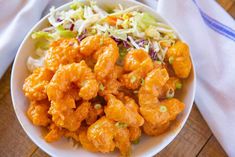 a white bowl filled with chicken and coleslaw next to a napkin on top of a wooden table