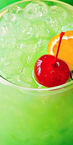 a green drink with an orange slice and a cherry garnish