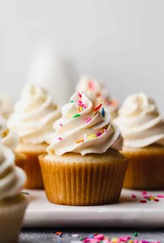 several cupcakes with white frosting and sprinkles on a plate