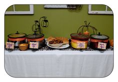 a table topped with lots of food next to a green wall and white table cloth