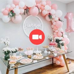 a table topped with pink and white balloons next to a glass table covered in cupcakes