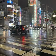 a busy city street at night with cars and people crossing the street in the rain