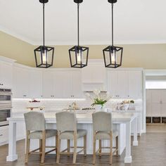 a kitchen with an island and four lights hanging from the ceiling, along with white cabinets