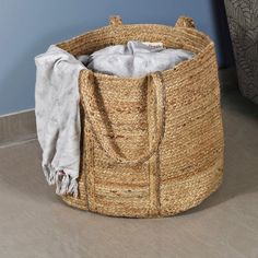 an empty basket sitting on the floor in front of a blue wall with a white blanket