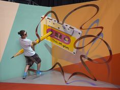 a man is holding a giant pencil in front of a wall with an advertisement on it