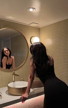 a woman standing in front of a bathroom mirror next to a sink and counter top