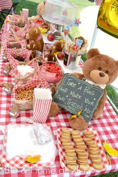 a teddy bear sitting at a picnic table with food and drink on it's side