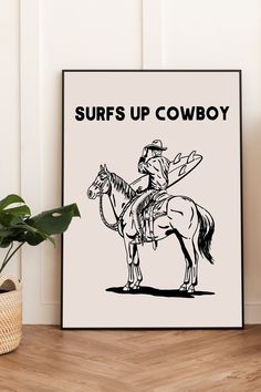 a black and white poster with the words surfs up cowboy on it next to a potted plant