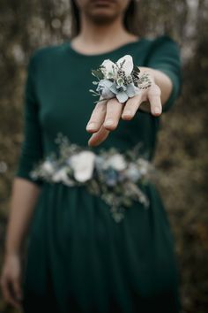 a woman in a green dress is holding out her hand with flowers on the wrist