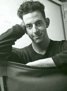 a black and white photo of a man leaning on a chair