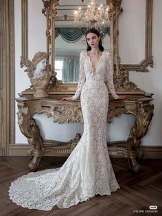 a woman standing in front of a mirror wearing a wedding dress with long sleeves and an open back