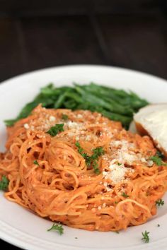 a white plate topped with pasta and green beans next to a piece of bread on top of a wooden table