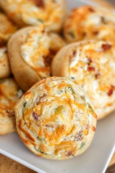 several small muffins on a white plate with cheese and other food items in the background