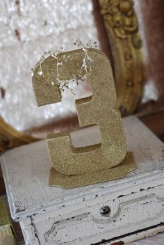 the number three is sitting on top of an old chest and it's gold glitter