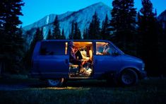 a van with the door open sitting in front of trees and mountains at night time