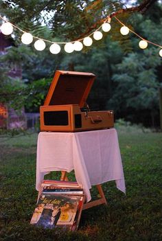 an open suitcase sitting on top of a table in the middle of a yard with lights strung above it