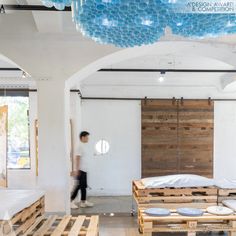 a man walking through a room with wooden pallets on the floor and blue balloons hanging from the ceiling