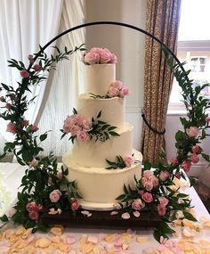 a white wedding cake with pink flowers and greenery on the top is surrounded by petals