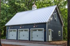 a blue garage with three doors and two lights on the roof, surrounded by trees