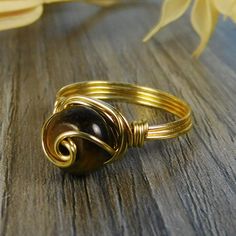 "Golden Tigers Eye Gemstone and Sterling Silver, Yellow or Rose Gold Filled Wire Wrapped Swirl Ring; Custom Made to Size ❀ This round golden tigers eye gemstone bead and wire wrapped ring is handmade with an approximately 8mm by 5mm bead and your choice of wire for the band. ❀ This ring (as well as all the others in my shop) is custom made to any size from 4 to 14 including half and quarter sizes! ❀ This ring can be made in Sterling Silver Filled Wire, Argentium Sterling Silver wire (tarnish res Hand Wrapped Round Jewelry For Anniversary, Adjustable Brown Jewelry For Anniversary, Handmade Adjustable Swirl Jewelry, Gold Wire Wrapped Swirl Jewelry, Wire Wrapped Swirl Jewelry As Gift, Gold Swirl Wire Wrapped Jewelry, Adjustable Nickel-free Swirl Jewelry, Hand Wrapped Gold Crystal Ring, Adjustable Swirl Ring As Gift