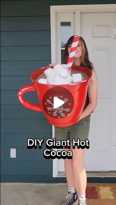 a woman holding a giant red cup filled with cotton in front of her face and the words diy giant hot cocoa on it