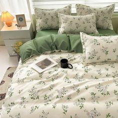 a bed with green and white sheets, pillows and a book on it in front of a window