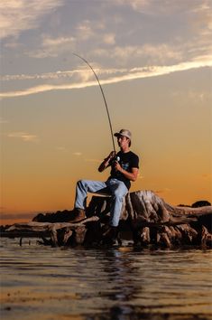 a man sitting on rocks holding a fishing pole