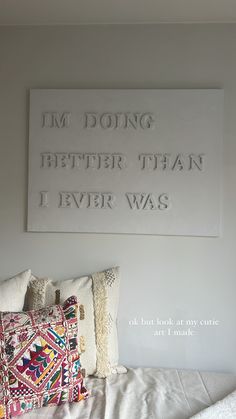 a bed topped with pillows next to a wall mounted art piece on the side of a wall