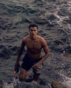 a shirtless man standing in the ocean holding a frisbee and looking at the camera