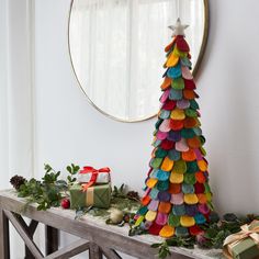 a brightly colored christmas tree sitting on top of a wooden table next to a mirror