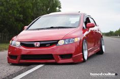 a red honda civic is parked on the side of the road with trees in the background