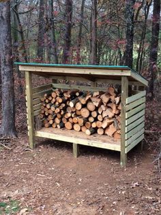 a pile of wood sitting in the middle of a forest next to a firewood shed